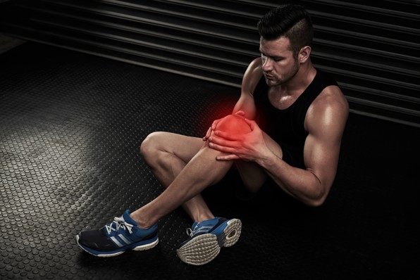 Man sitting on gym floor holding injured knee