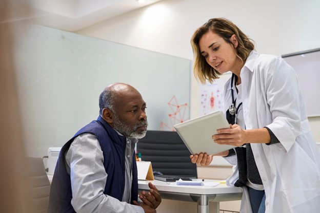 A person in a white coat holding a tablet and talking to a patient